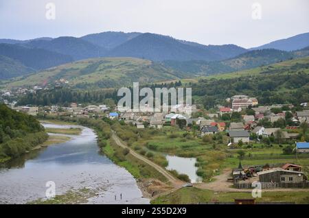 Eine wunderschöne Aussicht auf das Dorf Mezhgorye, Karpaten Region. Eine Menge von Wohngebäuden durch hohe Wald Berge und lange Fluss umgeben Stockfoto
