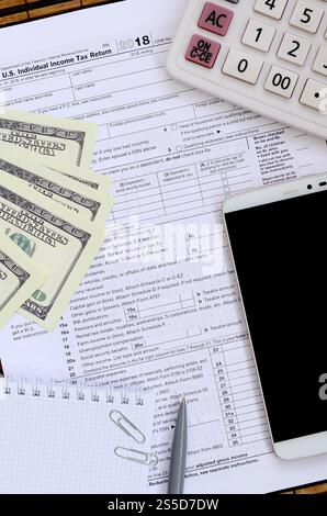 Zusammensetzung der Gegenstände, die auf dem Steuerformular 1040 liegen. Dollarscheine, Stift, Rechner, Smartphone, Büroklammer und Notizblock. Die Zeit, Steuern zu zahlen Stockfoto