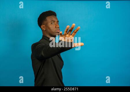 Junger Mann mit Stoppschild mit Handgeste, der Ablehnung oder Ablehnung auf blauem Hintergrund ausdrückt Stockfoto