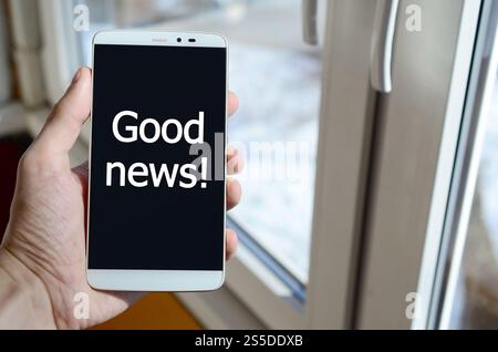 Eine Person sieht eine weiße Beschriftung auf einem schwarzen Smartphone-Display, das in der Hand hält. Gute Neuigkeiten! Stockfoto