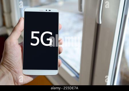 Eine Person sieht eine weiße Beschriftung auf einem schwarzen Smartphone-Display, das in der Hand hält. 5G Stockfoto