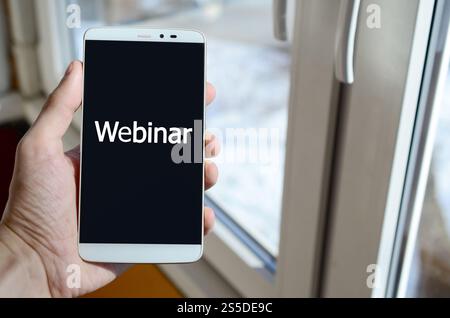 Eine Person sieht eine weiße Beschriftung auf einem schwarzen Smartphone-Display, das in der Hand hält. Webinar Stockfoto