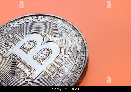 Schokoladenprodukt in Form von Bitcoin liegt auf einem orangefarbenen Kunststoffhintergrund. Modell der Kryptowährung in essbarer Form Stockfoto