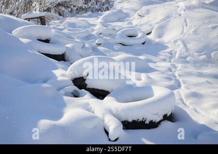 Gebrauchte und entsorgte Autoreifen liegen am Straßenrand und sind mit einer dicken Schneeschicht bedeckt Stockfoto