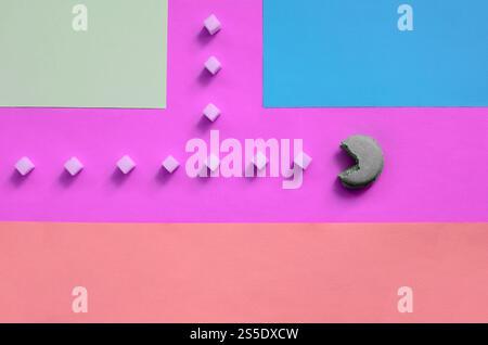 Eine Komposition aus Makronen mit offenem Mund, die Zuckerwürfel auf rosa, Limette, blau und korallenpastellfarbenen Hintergrund essen wird. Der Begriff des Alten Stockfoto