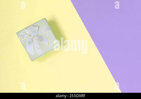 Kleine gelbe Geschenkbox liegt auf Textur Hintergrund von Mode Pastellgelb und violett Farben Papier in minimalem Konzept. Kleine gelbe Geschenkbox liegt drauf Stockfoto