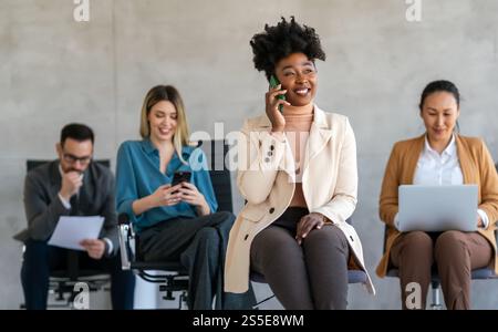 Geschäftiges, lächelndes Business-Team, das digitale Geräte im Büro nutzt. Vielfältige professionelle Mitarbeiter Stockfoto