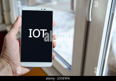 Eine Person sieht eine weiße Beschriftung auf einem schwarzen Smartphone-Display, das in der Hand hält. IOT Stockfoto