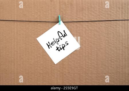 Hilfreiche Tipps. Die Notiz ist auf einem weißen Aufkleber geschrieben, der mit einem Kleiderschrank an einem Seil auf einem Hintergrund aus braunem Karton hängt Stockfoto