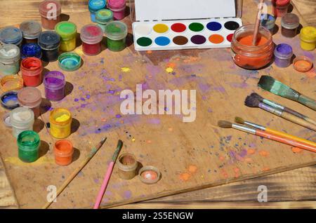 Stillleben, Interesse an Aquarellmalerei und Kunst. Viele Pinsel, Gläser mit Aquarellfarbe und gebrauchte Gouache liegen auf einem alten Holz Stockfoto