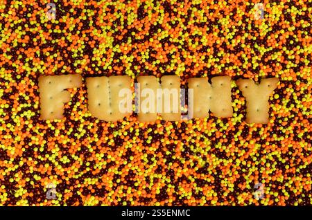 Lustig. Das Wort aus den eßbaren Cracker-Buchstaben liegt auf dem glasierten Pulver. Eine große Anzahl süßer, farbenfroher Perlen von sehr kleiner Größe zur Dekoration Stockfoto
