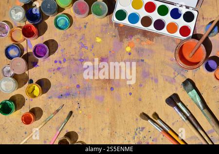Stillleben, Interesse an Aquarellmalerei und Kunst. Viele Pinsel, Gläser mit Aquarellfarbe und gebrauchte Gouache liegen auf einem alten Holz Stockfoto