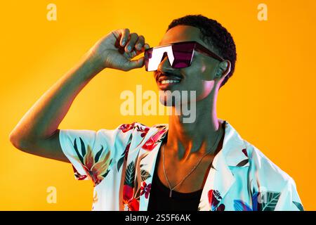 Afrikanischer Mann junger Porträt im Studio auf bunter Hintergrund - cooler schwarzer junger Mann mit stilvoller Kleidung posiert, kreative farbige Beleuchtung Stockfoto