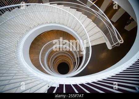 Wendeltreppe mit weißen Brüstungen, die in die Dunkelheit hinabsteigen, von oben in der Universitätsbibliothek von Helsinki gesehen Stockfoto