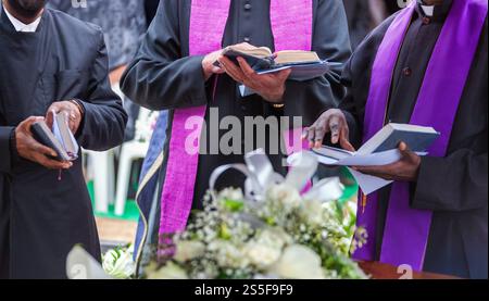 Drei Priester, die bei einer Beerdigung Gebete aus der Bibel lesen, um das Grab zu segnen. Stockfoto