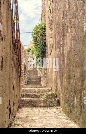 Schmale Steintreppe mit Wänden auf beiden Seiten, die zwischen alten Gebäuden unter klarem blauen Himmel nach oben führen, Mali Ston, Kroatien Stockfoto