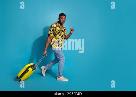 Junger Mann in lebendigem Hemd, der mit Koffer reist und die Sommerpause auf auffälligem blauem Hintergrund genießt Stockfoto