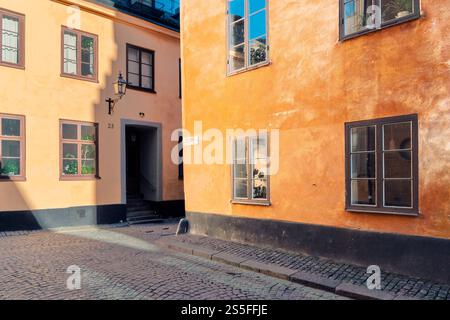 Sonnenlicht wirft Schatten auf die farbenfrohen Fassaden traditioneller Gebäude in einer bezaubernden Kopfsteinpflasterstraße in Gamla Stan, Stockholm, Schweden Stockfoto