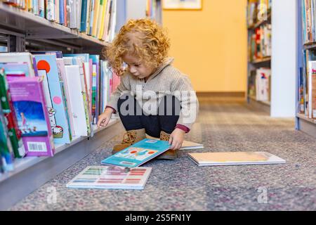 Ein lockiges Kind, das vertieft ist, ein Buch auf dem Boden eines bunten Bücherschiffs zu lesen. Cleveland, Ohio, USA Stockfoto
