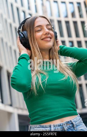 Lächelnde junge Frau, die Musik über Kopfhörer in der Stadt genießt, Berlin, Deutschland Stockfoto