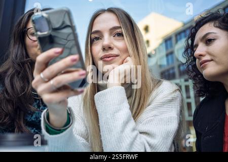 Drei Freunde, die gemeinsam ein Smartphone benutzen, lächeln und sich mit dem beschäftigen, was sie auf dem Bildschirm sehen, Berlin, Deutschland Stockfoto