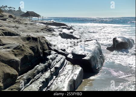 Wellen brechen an einem sonnigen Strand in New Orleans, USA, unter einem klaren blauen Himmel an der felsigen Küste ab Stockfoto