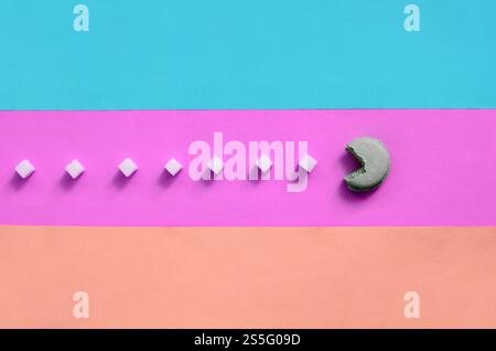 Eine Komposition aus Makronen mit offenem Mund, die Zuckerwürfel auf rosa, Limette, blau und korallenpastellfarbenen Hintergrund essen wird. Der Begriff des Alten Stockfoto