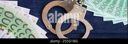 Der Fan von vielen Euro-Scheinen und Polizeihandschellen ist auf einer dunklen Jeansfläche. Hintergrundbild Stockfoto
