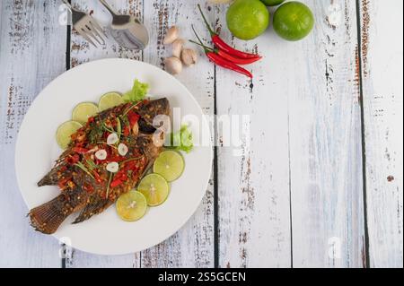 Gebratene Tilapia mit Chili-Sauce, Zitronensalat und Knoblauch auf einem Teller auf einem weißen Holztisch. Stockfoto