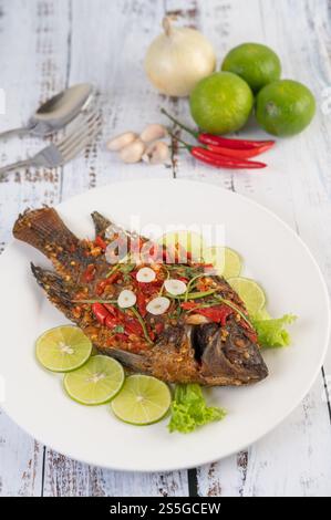 Gebratene Tilapia mit Chili-Sauce, Zitronensalat und Knoblauch auf einem Teller auf einem weißen Holztisch. Stockfoto