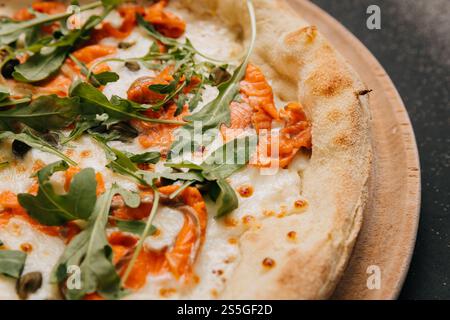 Gourmet-Pizza mit Räucherlachs, Rucola und Kapern auf einem Holzbrett für eine köstliche Mahlzeit Stockfoto