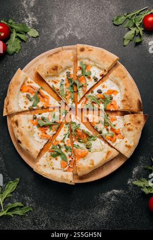 In Scheiben geschnittene Gourmet-Pizza mit Räucherlachs, Rucola und Kapern auf einem Holzbrett für ein stilvolles fest Stockfoto