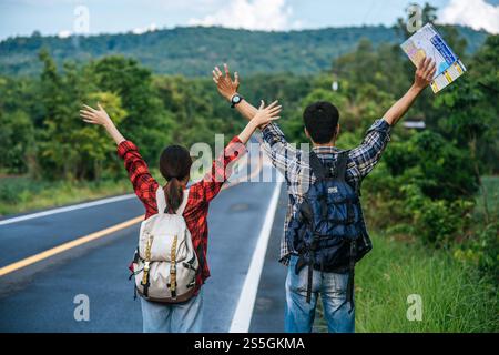 Sowohl männliche als auch weibliche Touristen tragen einen Rucksack, stehen auf der Straße und heben die Hände auf beiden Seiten. Stockfoto