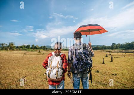 Sowohl männliche als auch weibliche Touristen tragen einen Rucksack, der auf dem Rasen steht und Männer Regenschirme verteilen. Stockfoto