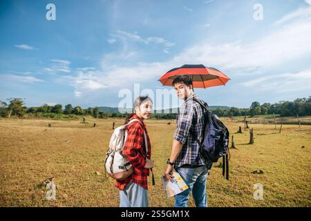 Sowohl männliche als auch weibliche Touristen tragen einen Rucksack, der auf dem Rasen steht und Männer Regenschirme verteilen. Stockfoto