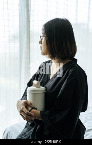 Die Frau trägt ein schwarzes Gewand und umarmt Tiffin und schaut nach draußen. Stockfoto