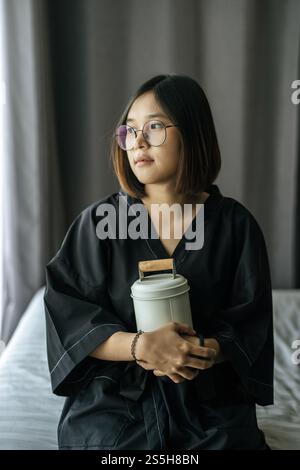 Die Frau trägt ein schwarzes Gewand und umarmt Tiffin und schaut nach draußen. Stockfoto