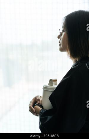 Die Frau trägt ein schwarzes Gewand und umarmt Tiffin und schaut nach draußen. Stockfoto