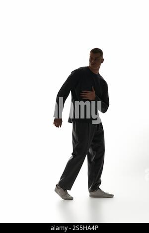 Ein gutaussehender junger Mann posiert dynamisch vor einer hellen, minimalen Kulisse und strahlt Charme aus. Stockfoto