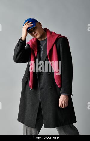 Ein junger Mann trägt selbstbewusst einen stilvollen Mantel und einen lebendigen Schal in einem minimalistischen Raum. Stockfoto