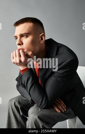 Ein hübscher junger Mann legt sein Kinn auf seine Hand, tief nachdenklich vor einem eleganten Hintergrund. Stockfoto