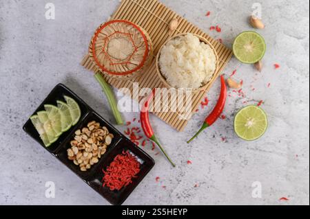 Thailändischer Kleberreis in einem gewebten Bambuskorb auf einer Holzplatte mit Chilis, Limette und Knoblauch. Draufsicht. Stockfoto