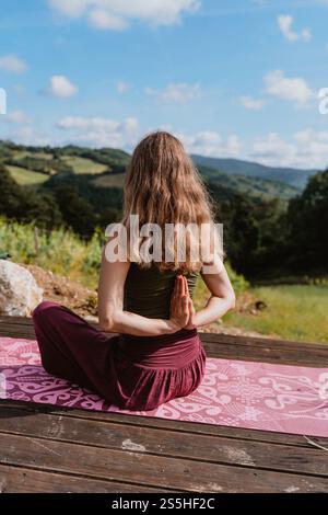 Junge Frau, die im Freien Yoga macht, vor hügeliger Landschaft. Konzept der Morgenentspannung auf Naturhintergrund Stockfoto