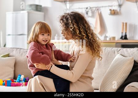 Die lockige Mutter und ihre fröhliche Tochter teilen an einem gemütlichen Nachmittag Lachen und Freude. Stockfoto