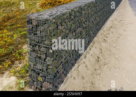 Moderne Entwicklung der Strandpark-Umwelteinrichtungen, Gabionenzaun-Wand aus Stahlgitter gefüllt mit Steinen, die die Bewegung von Dünensand einschränken Stockfoto