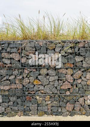 Moderne Entwicklung der Strandpark-Umwelteinrichtungen, Gabionenzaun-Wand aus Stahlgitter gefüllt mit Steinen, die die Bewegung von Dünensand einschränken Stockfoto