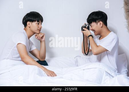 Zwei geliebte junge Männer saßen auf dem Bett und machten Fotos mit der Kamera. Stockfoto