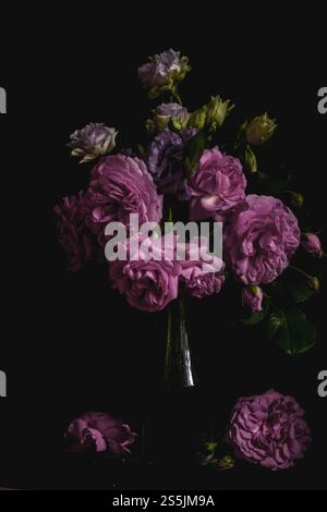 Stillleben. Luxuriöse Blumenstrauß-Rosen und Lisianthus in einer Glasvase auf schwarzem Hintergrund. Moody Blumen. Farbblüte. Stockfoto