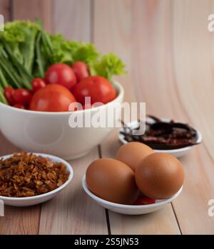 Gebratene Zwiebeln, Paprika, Eier, Tomaten, Salat und Frühlingszwiebeln in einer weißen Tasse auf Holzboden. Stockfoto