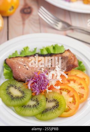 Fischsteak mit Pommes frites, Kiwi, Salat, Karotten, Tomaten, und Kohl in einer weißen Schale Stockfoto